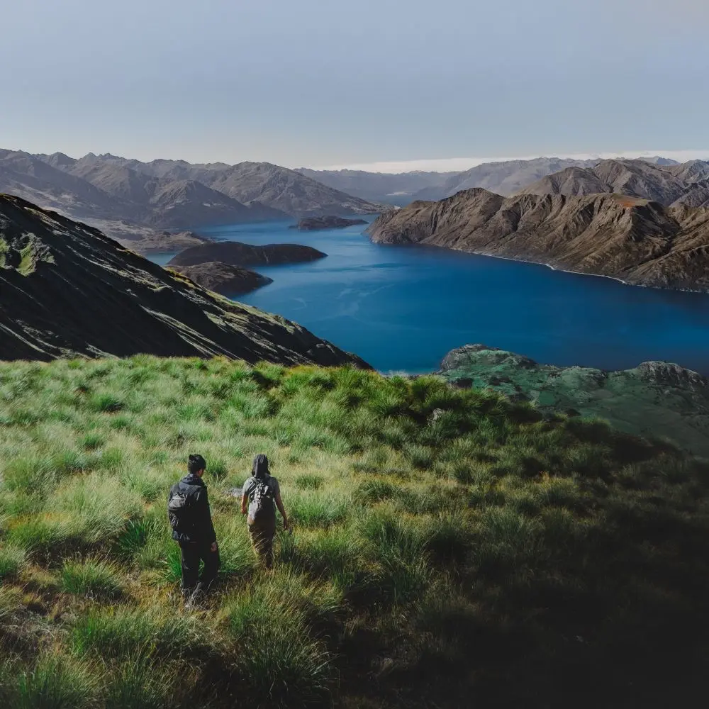 Zwei Wanderer auf Wiese, im Hintergund Fjord und kahle Berge